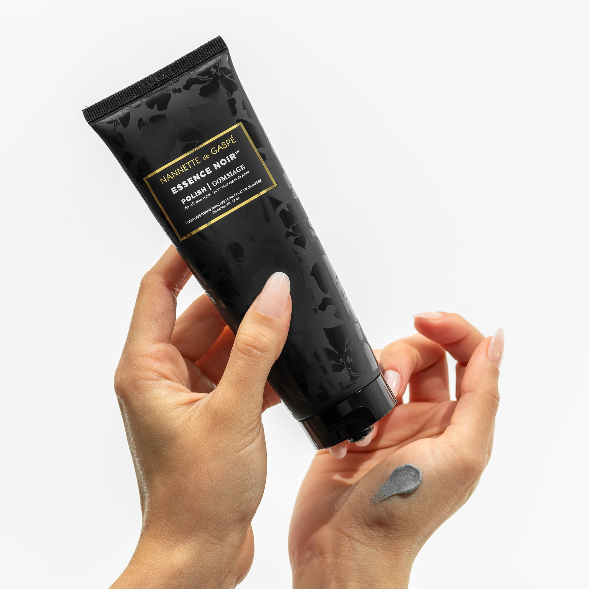 Applying Essence Noir Polish black tube in hand with grey swatch, designed to smooth and refine skin
