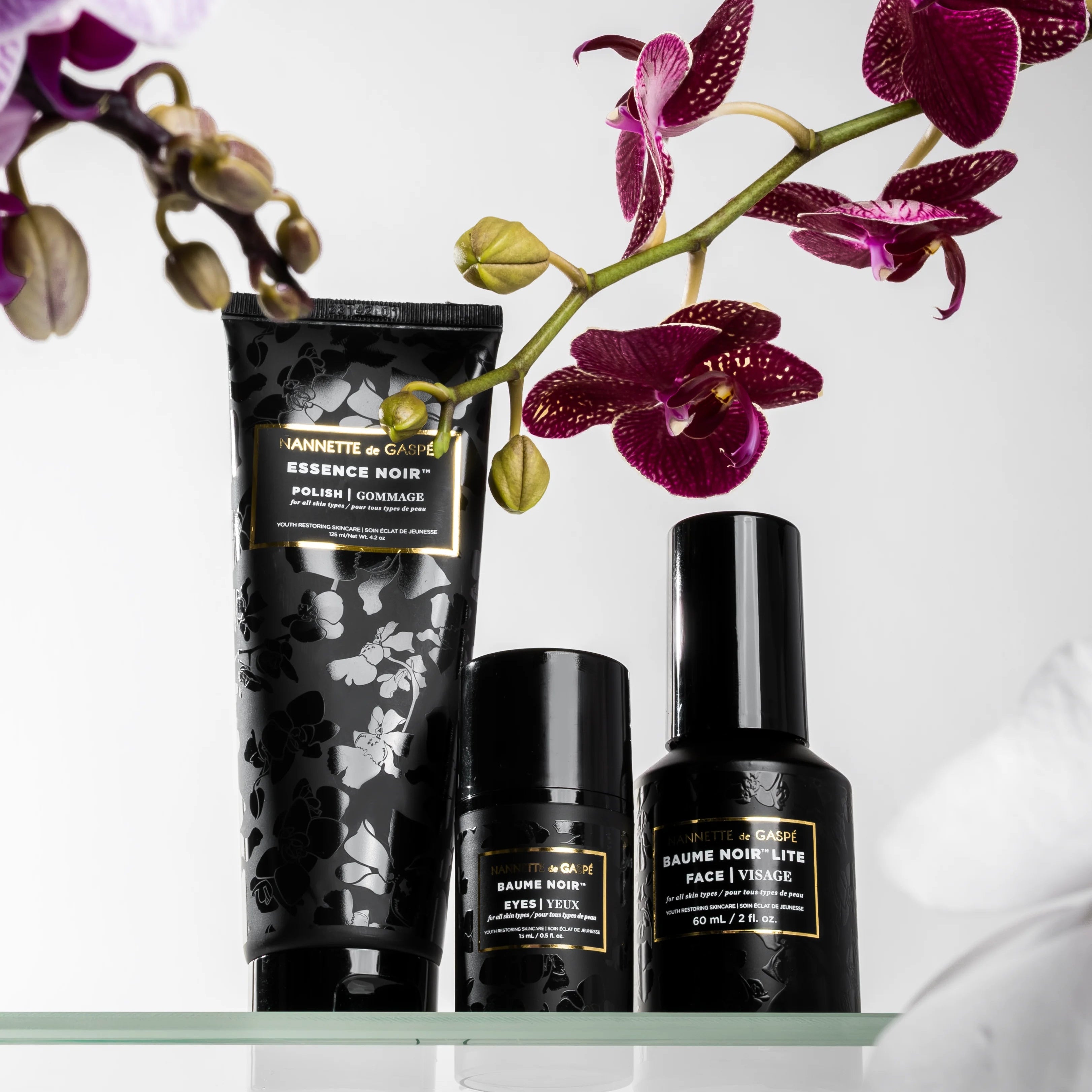 luxury skincare products with gold text on a white background with purple flowers.